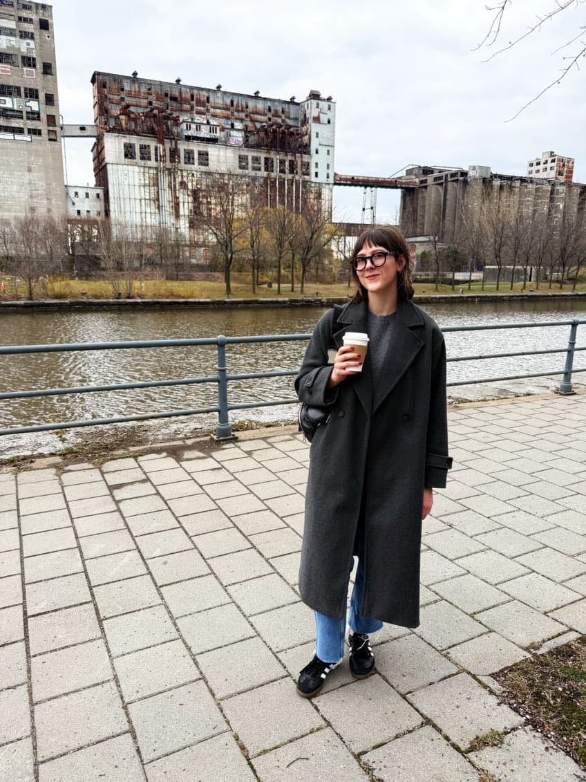 Photo of Sabrina smiling and holding a coffee by the canal in Montreal